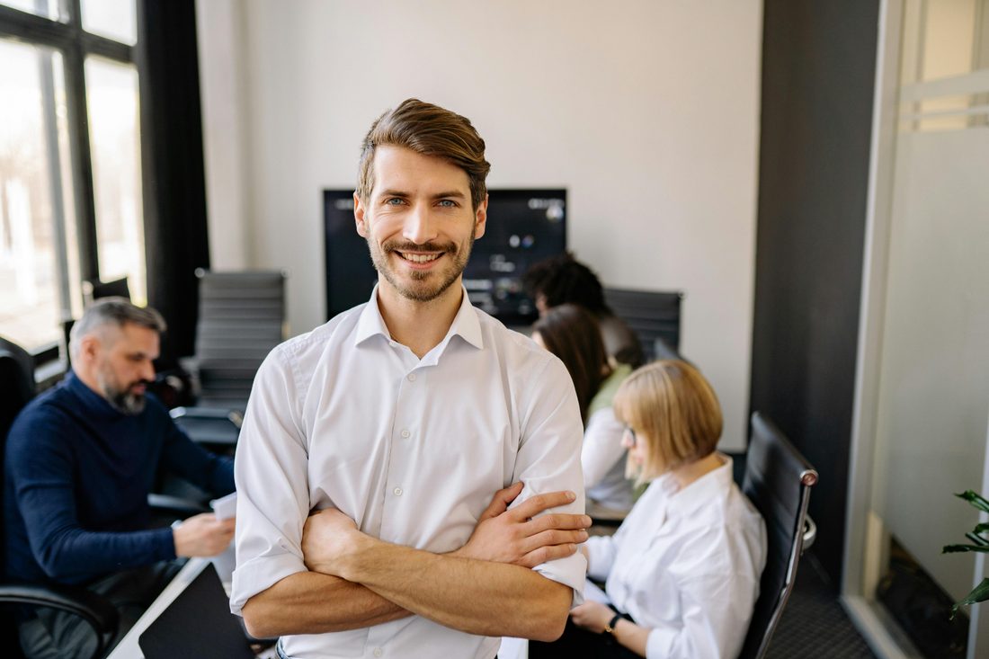 Confident Salesforce consultant with arms crossed, team working in the background